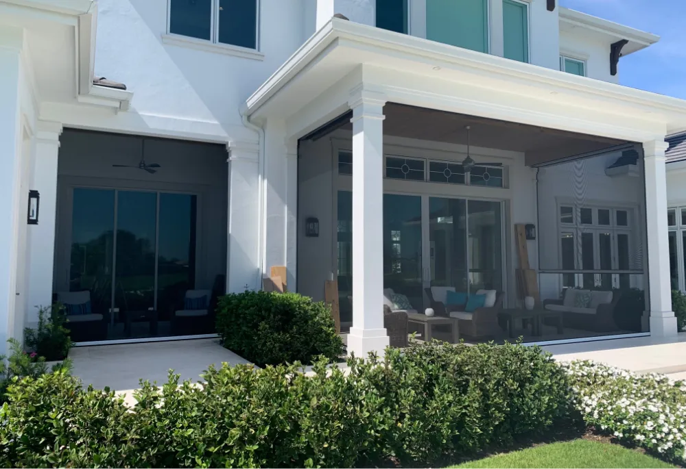 A luxurious backyard featuring a swimming pool with blue water, surrounded by a paved patio: An open patio cover overlooks the pool, connected to a modern house with large sliding doors and an outdoor seating area protected by retractable motorized screens.