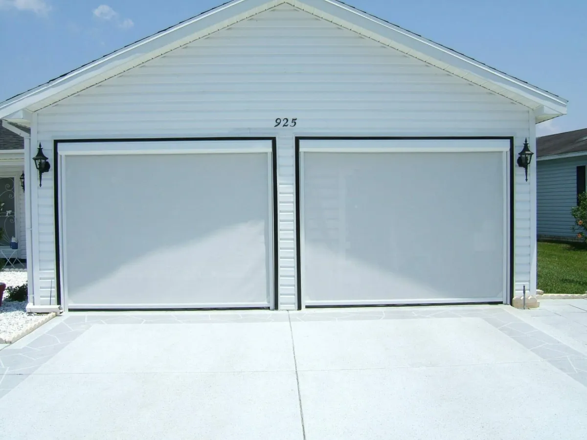 A double garage door with two FL Outdoor Motorized Screens mount on the outside of this spanish style home. 