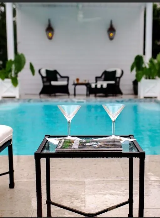 Two martini glass sitting on a wire frame table.  In the back ground is a white  aluminum privacy with two black coachman lights