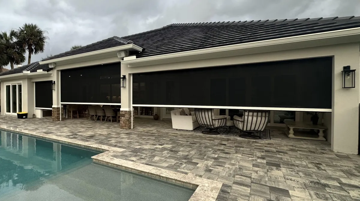 A photo of a home with Defender Motorized Screens half open.  The sky is ominous gray. 