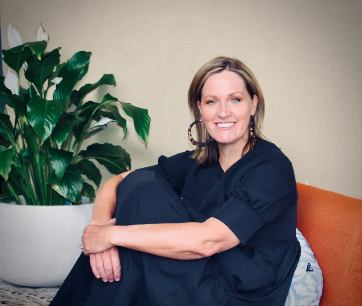 Tanya Somerton Author and Chief Review Office At Reviewly sitting on an orange chair in a blue dress, smiling.