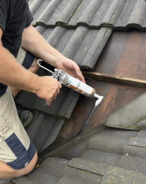 Applying white sealant to cracked roof flashing during leak repair on a concrete tile roof