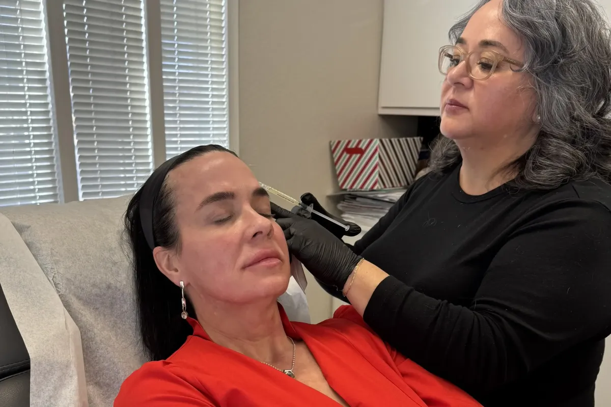 Gloved medical professional carefully administers a cosmetic injection to the face of a relaxed woman with eyes closed.