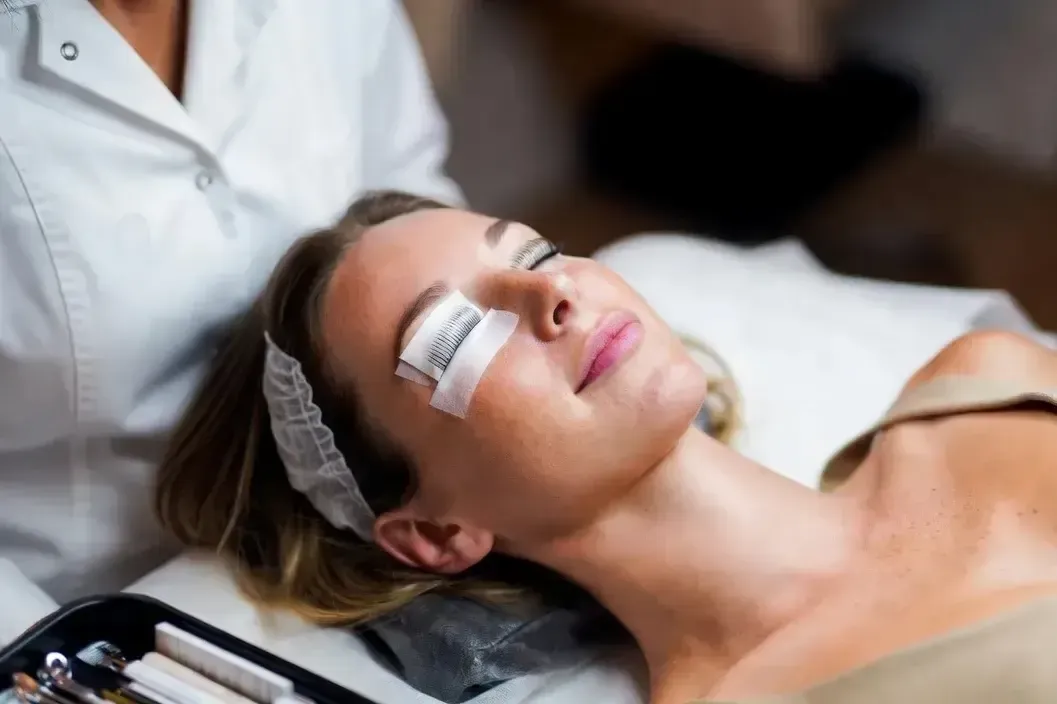 Woman receives a lash lift and tint treatment with white shields on her eyelids during a professional beauty service.