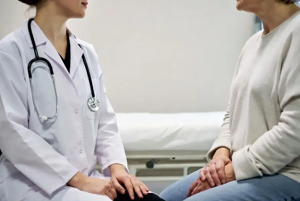 Female healthcare provider in a white coat holds hands with a patient during a compassionate hormone optimization consultation in a clinical setting.