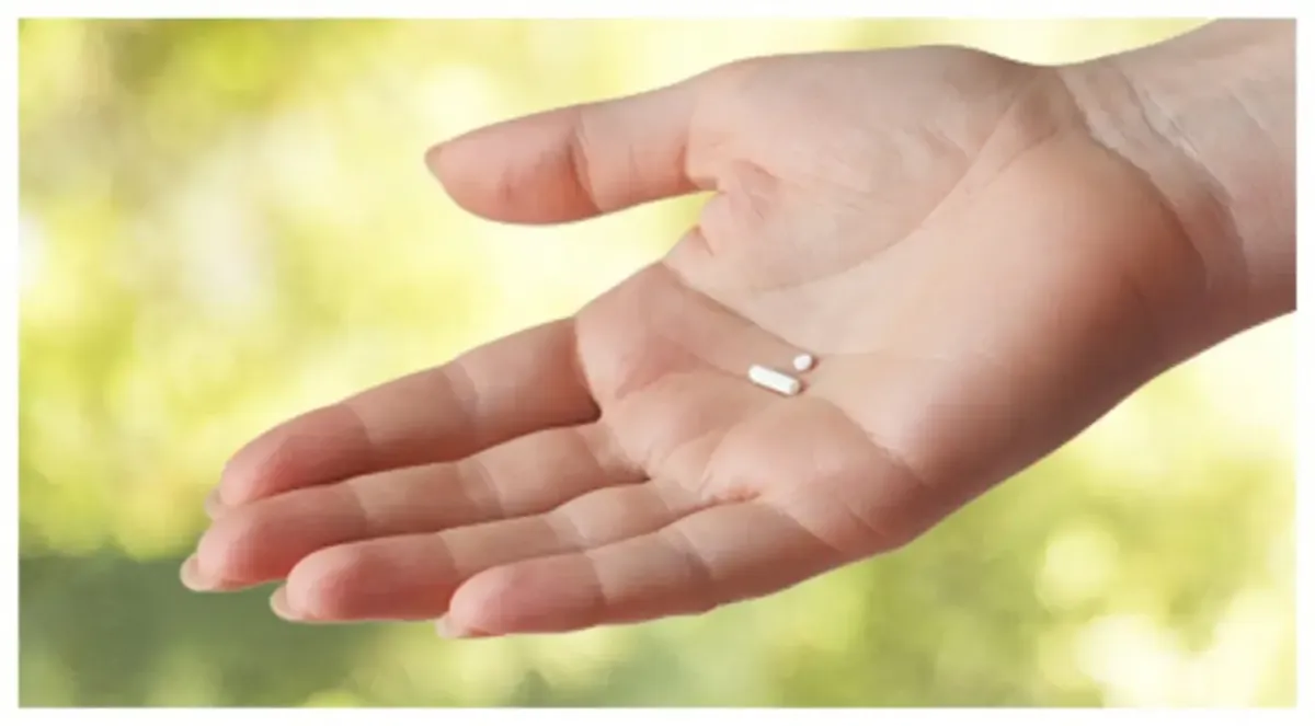 Close-up of a woman's hand holding two small BioTe hormone pellets used for female pellet therapy.