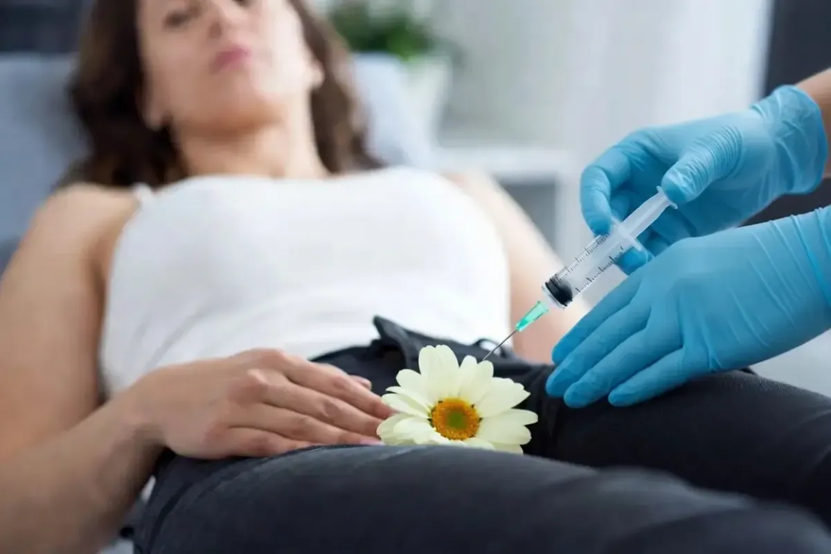 Gloved medical professional administers an injection for vaginal restoration treatment, with a flower placed for visual discretion.