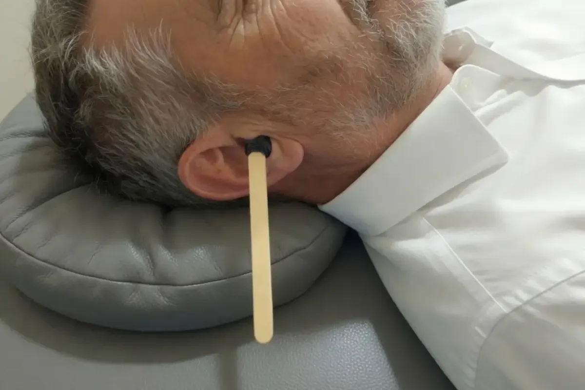 Man lying on his side with a wooden ear cleaning tool inserted into his ear during an ear wax removal treatment.