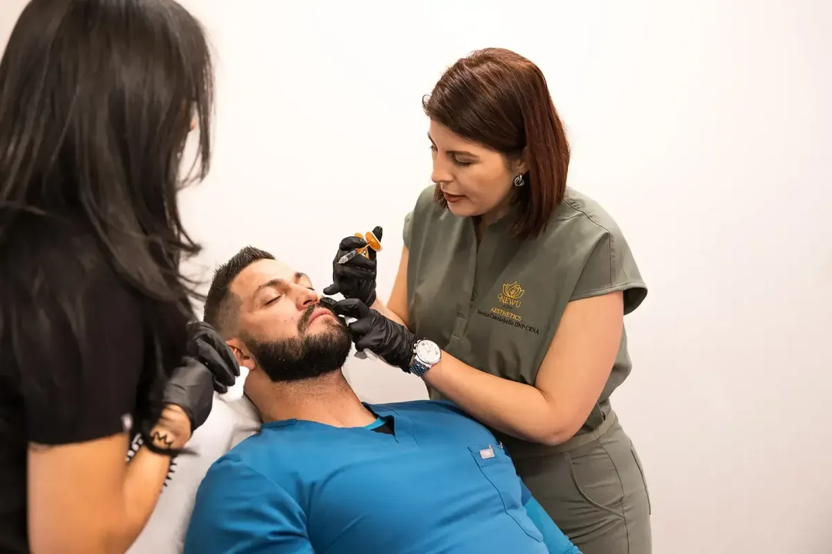 Aesthetic instructor (in black) teaching dermal filler injection technique to a trainee performing the procedure on a male patient during a hands-on training session at Chrome Aesthetics Academy.