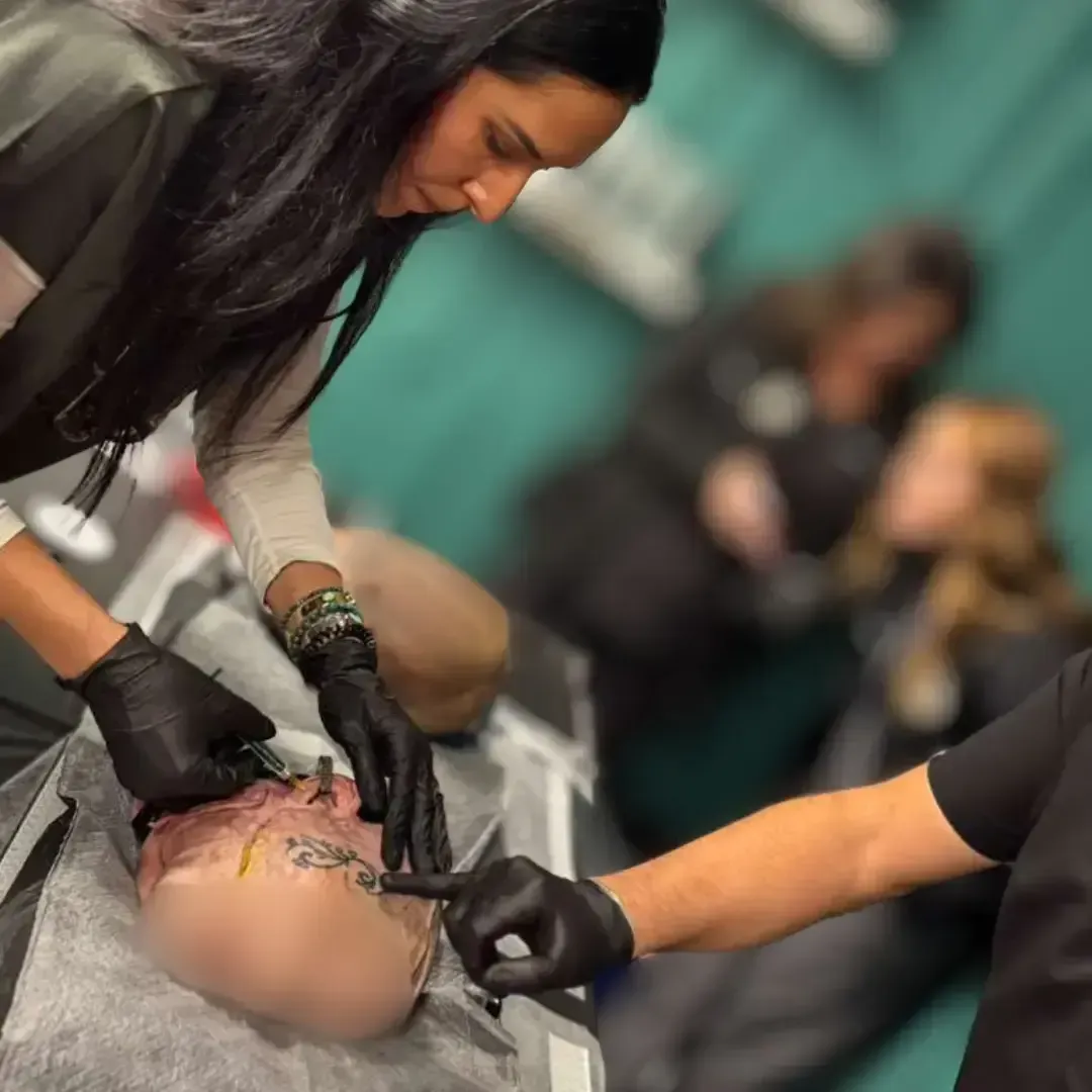 Hands-on facial anatomy training during a cadaver lab session, with instructors demonstrating injection points on a cadaver head at Chrome Aesthetics Academy.