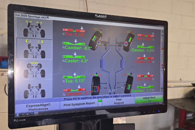 Wheel alignment screen displaying front and rear wheel camber, caster, and toe measurements in green and red during a professional alignment service.