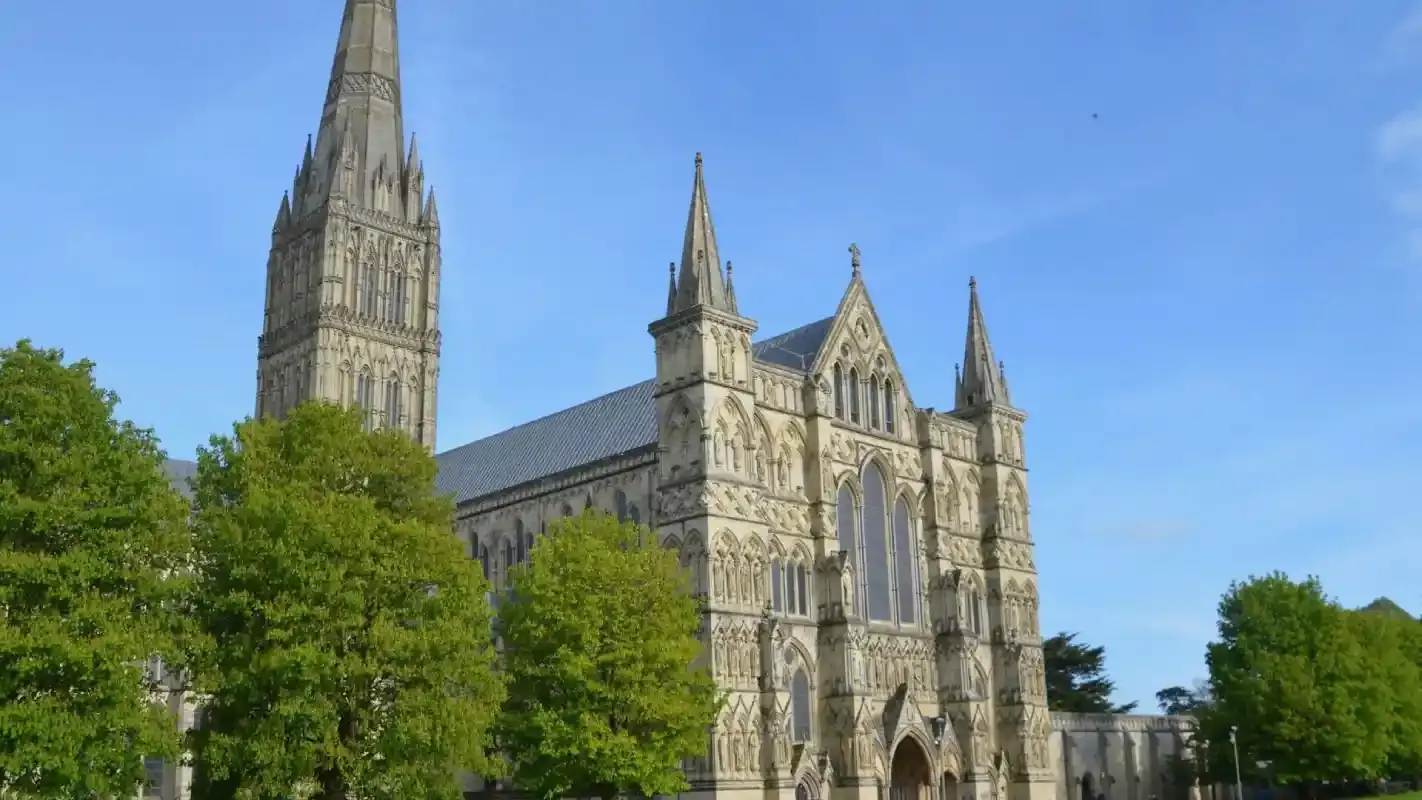 Historic Gothic cathedral with tall spires surrounded by green trees under a clear blue sky