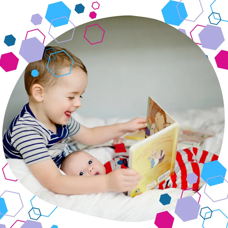 newborn baby lying on a bed in big brother's lap whilst the older boy shares a book with the baby. CubCare refresher antenatal classes.