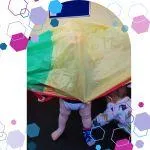 Image of a toddler hiding and playing a game under a parachute in a CubCare Active Play class.