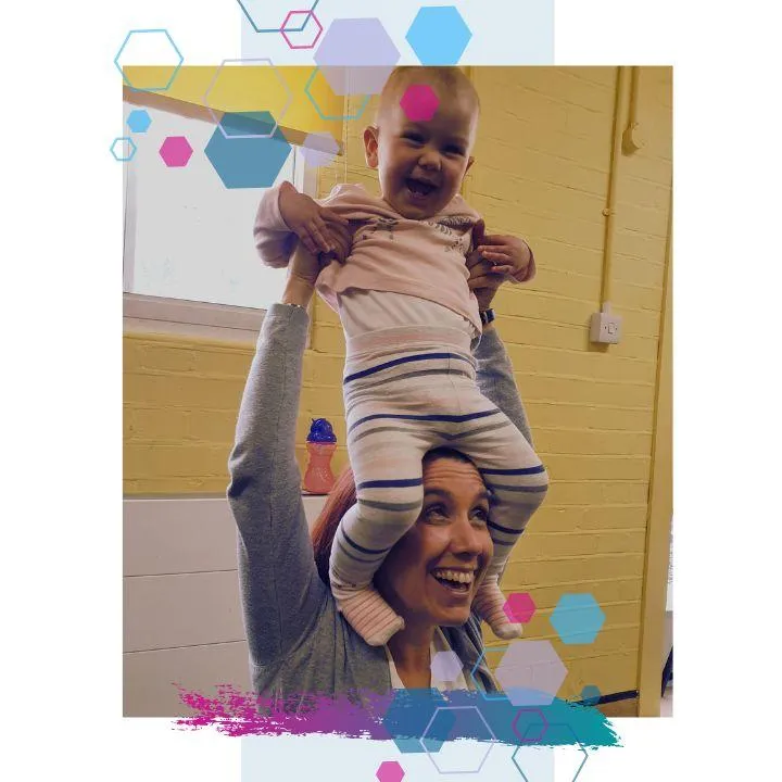 A mum smiling with her baby sitting on her head. The baby is smiling looking at the camera at a CubCare Wrigglers Baby Yoga and Sensory class in Welwyn Hatfield