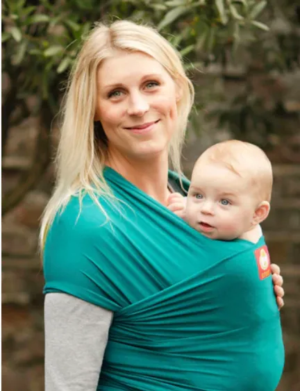 Hana Baby Stretchy Wrap image. Mum smiling at the camera whilst wearing her baby in a stretchy wrap hired from Welwyn Slings.