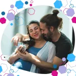 Pregnant woman smiling while holding baby booties, supported by her partner — testimonial image for the CubCare Birth Partner Course, capturing early pregnancy excitement and connection.