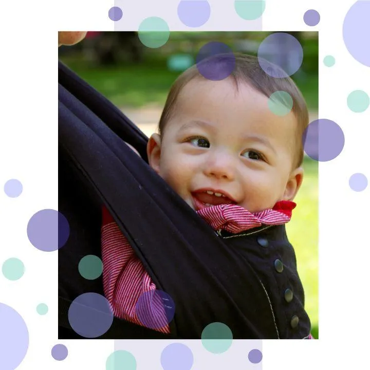 Smiling baby in a soft structured carrier during a babywearing demonstration outdoors. Image used for Welwyn Slings' professional training for nurseries, childminders, and health professionals on safe sling use.
