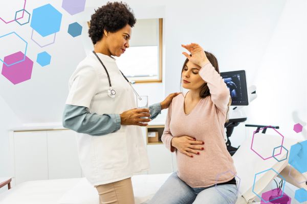 Pregnant person sitting on an examination table holding their abdomen and forehead while a clinician offers support, illustrating dizziness and lightheadedness that can occur in pregnancy with POTS and hypermobility.