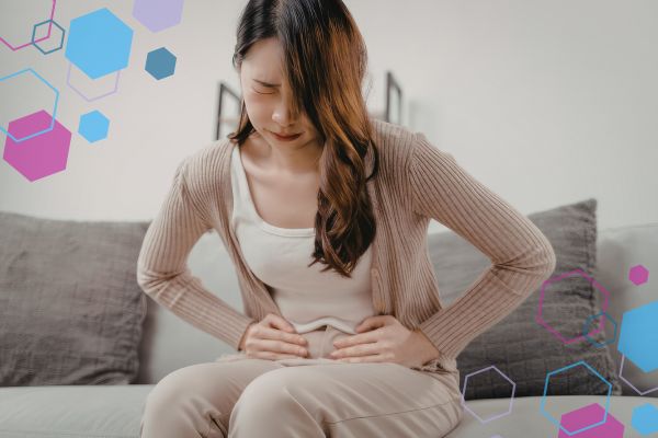 Person sitting on a sofa holding one side of their lower abdomen, illustrating one-sided abdominal pain that can occur in early pregnancy.