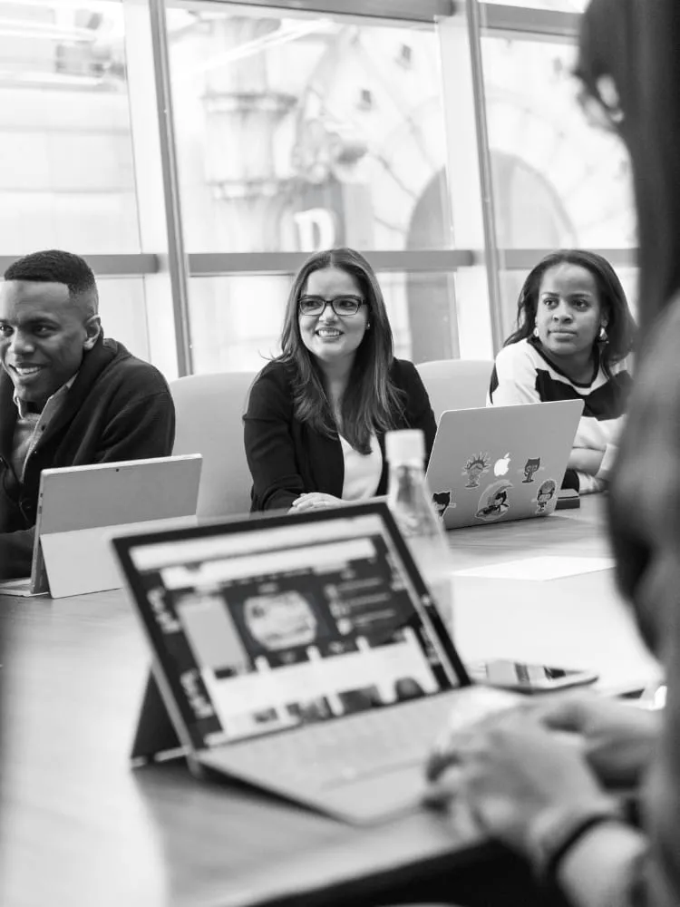 Black-and-white photo of colleagues seated around a table, with a laptop in the foreground.