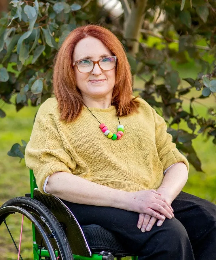 Ainslee Hooper seated in her wheelchair in a garden, wearing a yellow top
