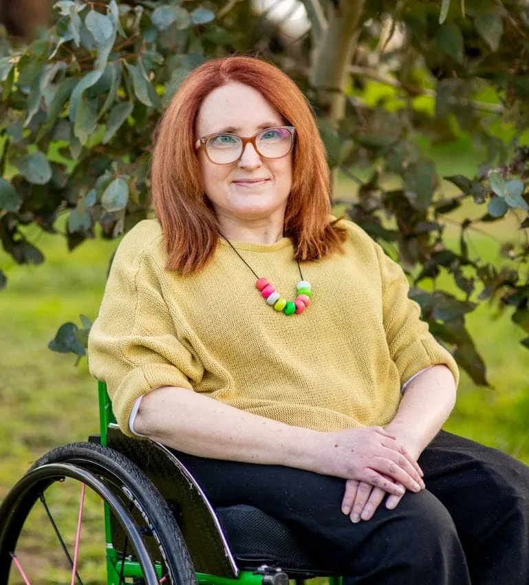 Ainslee Hooper smiling, seated in her wheelchair in a garden