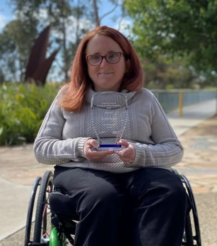 Ainslee Hooper in her wheelchair outdoors, holding an award