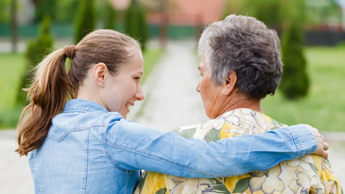 Young caregiver sitting outdoors with an older woman, offering companionship and support.