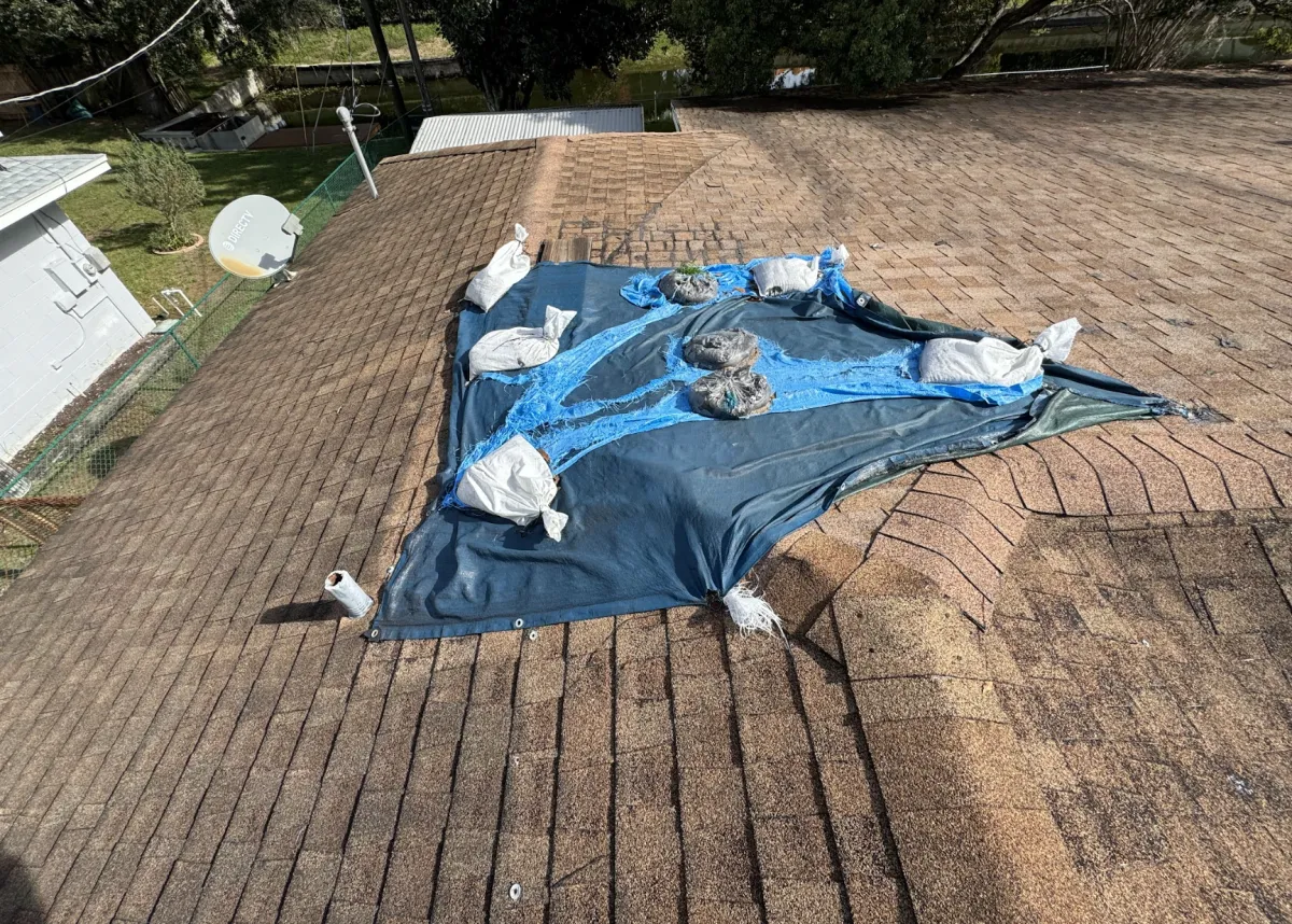 Temporary blue tarp covering damaged shingle roof to prevent water intrusion before repair.