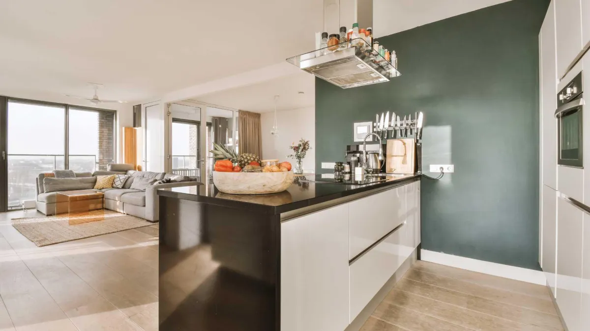 Modern kitchen with black and white cabinetry, a bowl of fresh fruit, and a cozy living area visible in the background, emphasizing inviting home staging for increased curb appeal.