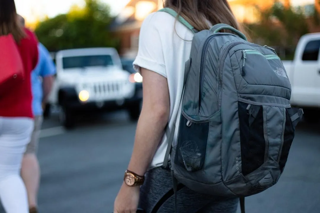 adolescent long-haired student with backpack walking in parking lot