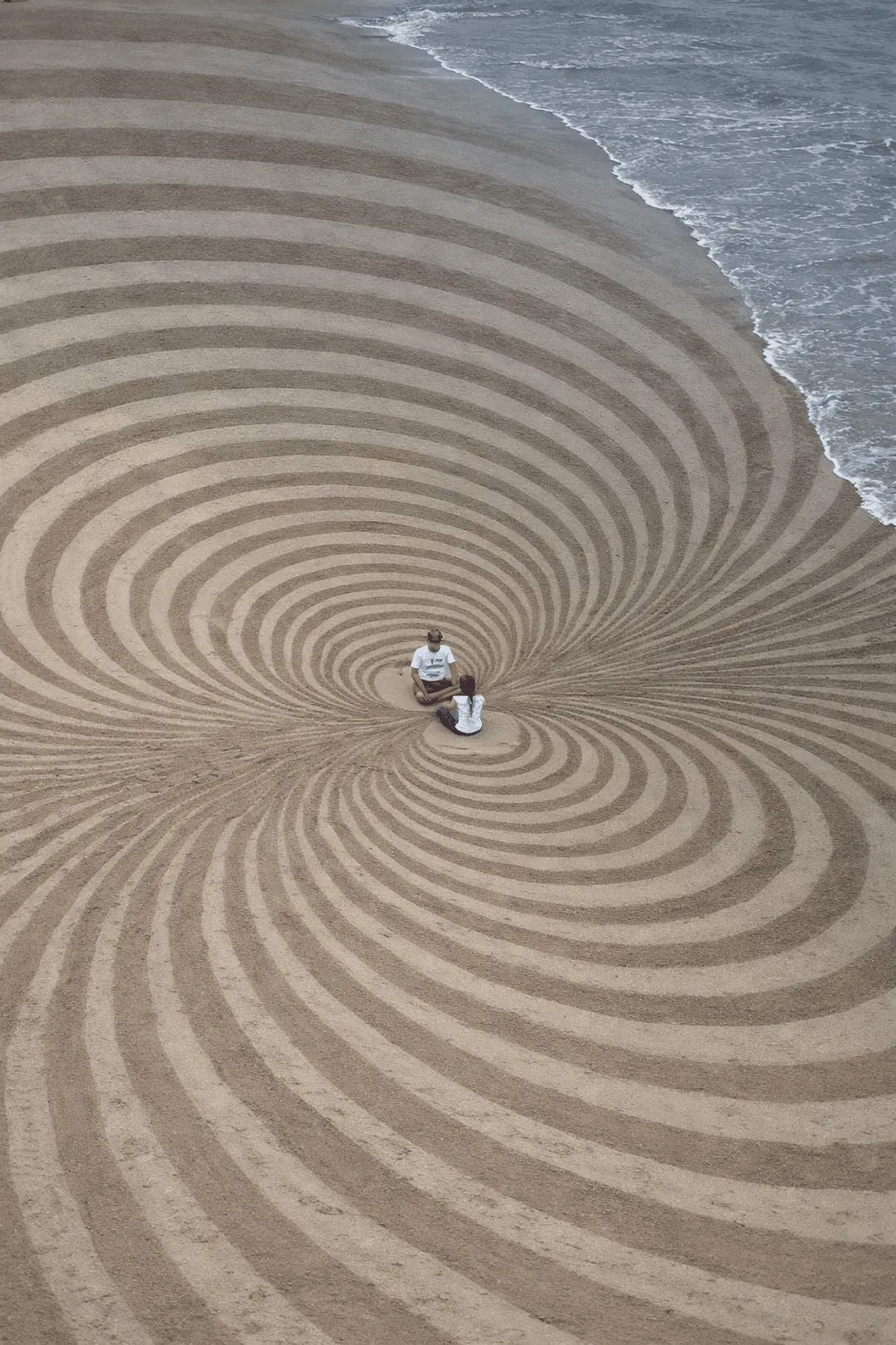 Personas sentadas en una espiral dibujada en la arena junto al mar