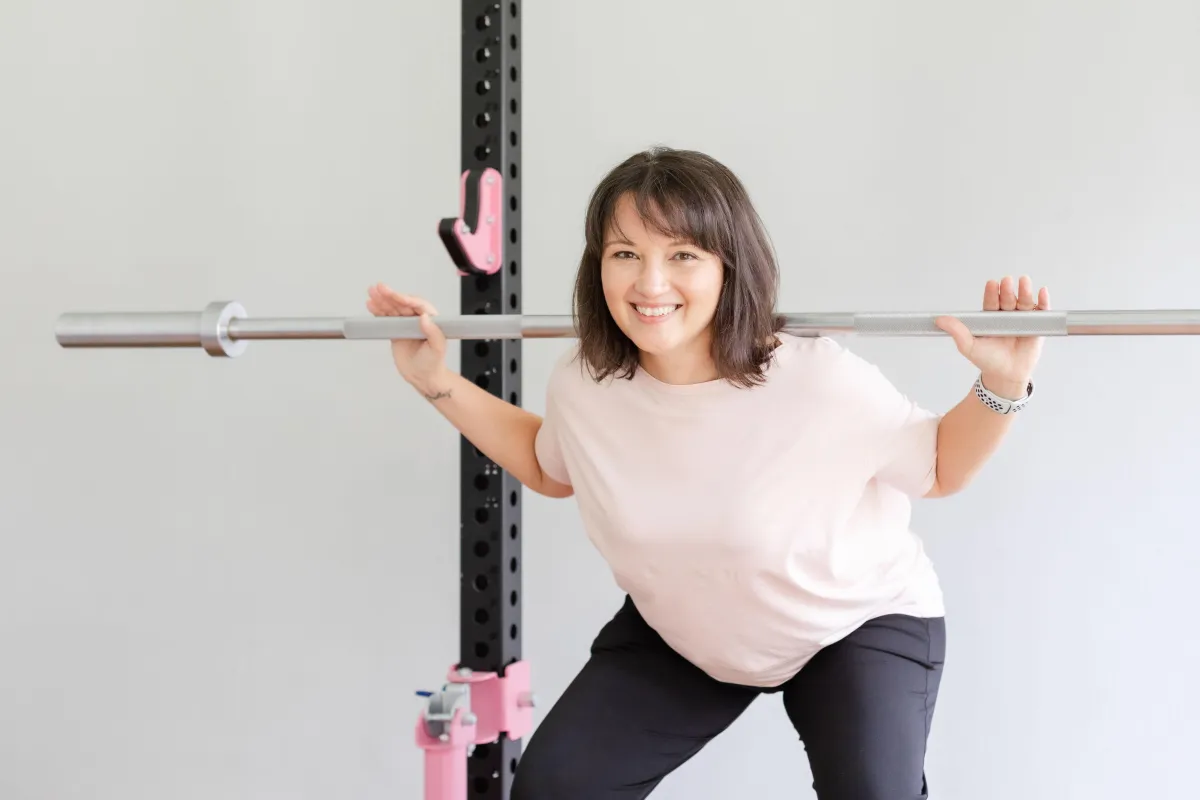 Woman in her 40s with a barbell across her back doing a squat, smiling at FitNut Loft Singapore