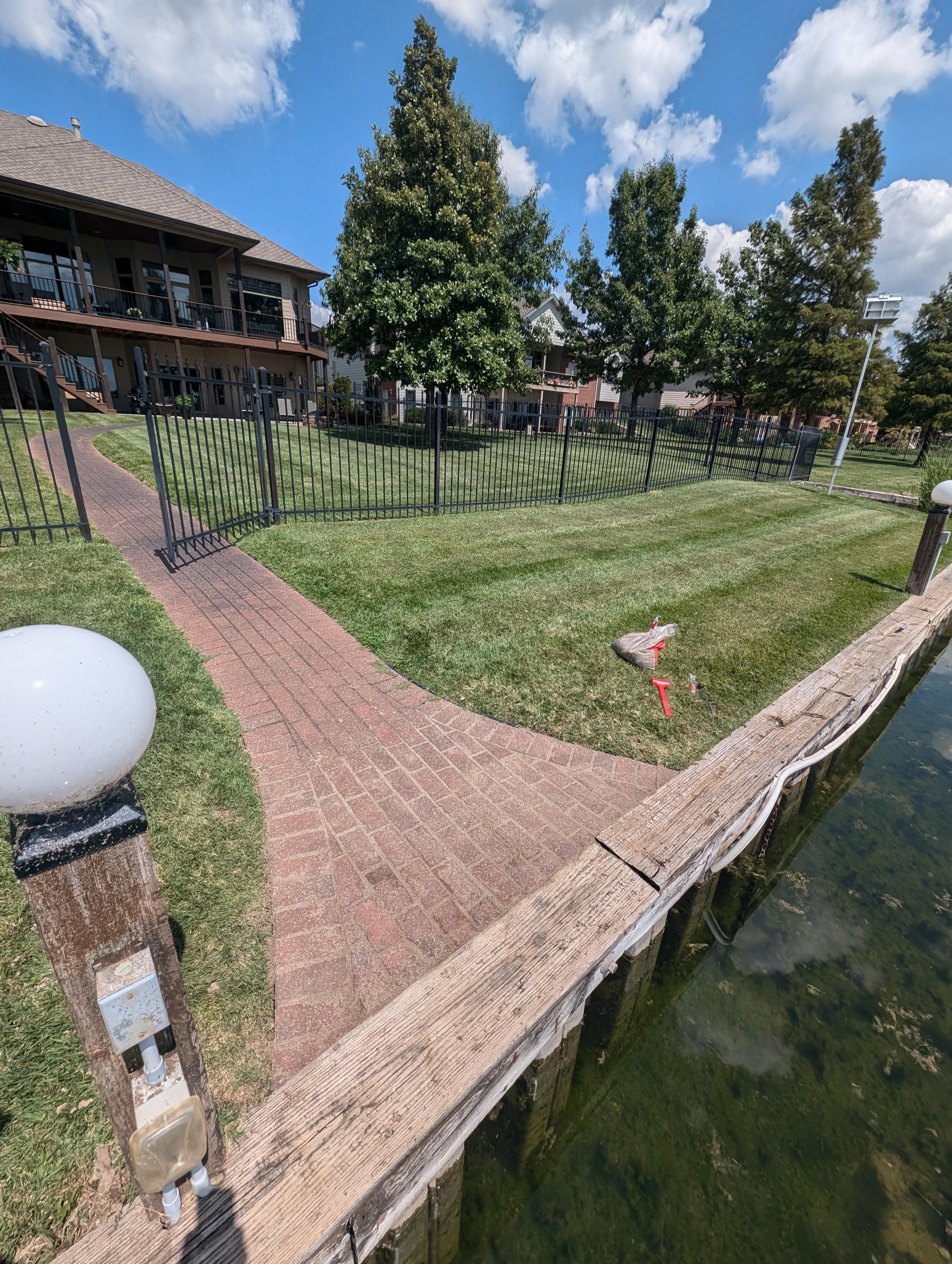 Pathway leading to a fenced yard with a well-maintained lawn, surrounded by trees and a waterfront, showcasing the outdoor space and landscaping services offered by My Handyman of Wichita.