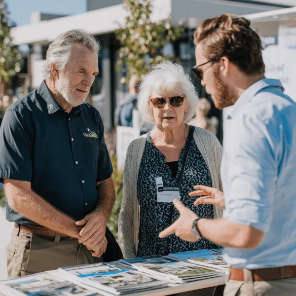 Building consultant speaking with a couple at an outdoor display, reviewing home brochures and discussing building options in a residential setting