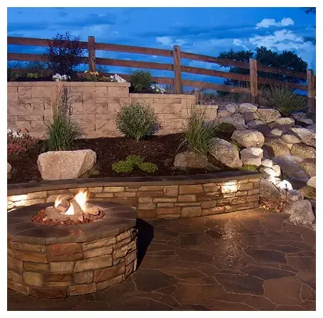 A built-in outdoor fire pit with a blazing fire, surrounded by rocks and vegetation