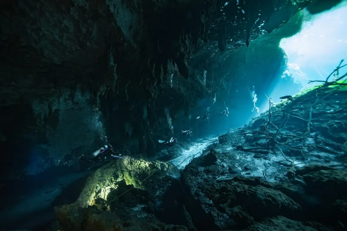 Group of scuba divers exiting the cavern section at Car Wash cenote and heading to the sunbathed lagoon area. 