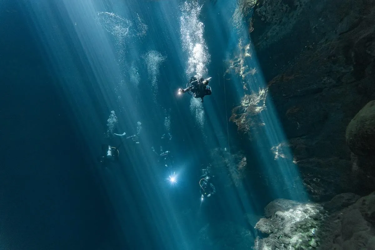 Diver descending through light beams in El Pit cenote
