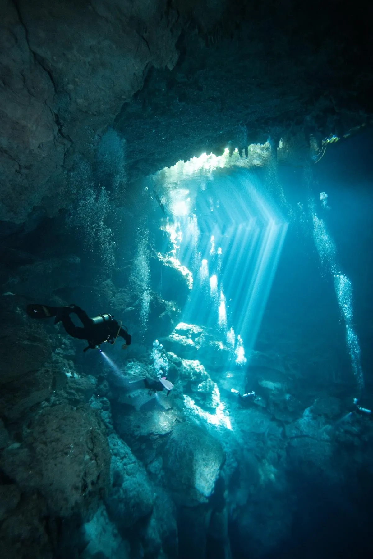 Silhouette of a scuba diver admiring the light beams penetrating El Pit Cenote near Tulum.