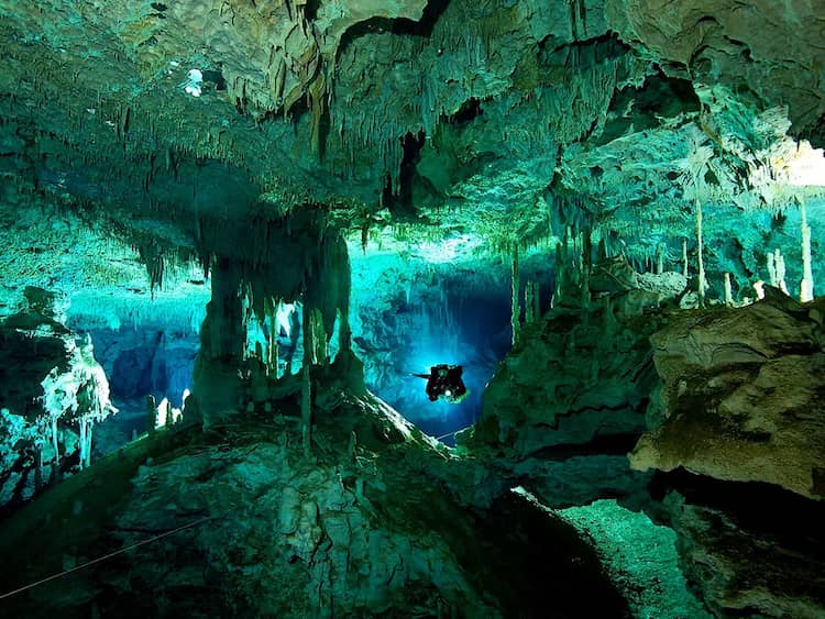 diver silhouette in dos ojos cenote surrounded by stalagmites and stalactites