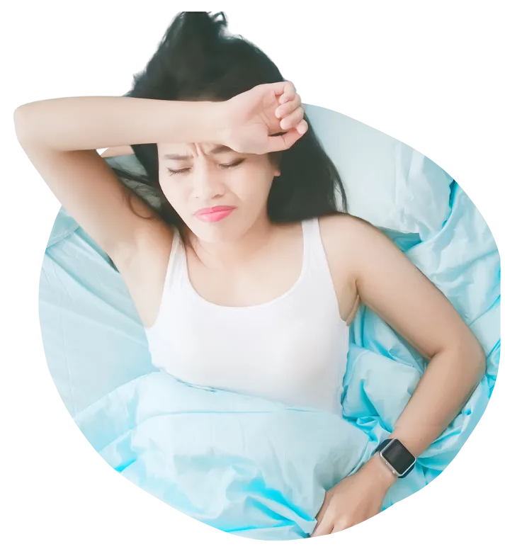 A woman in a white tank top lying in bed with light blue sheets, appearing to be in physical distress or unable to sleep. She has her eyes closed and her right arm draped over her forehead, with a pained facial expression.