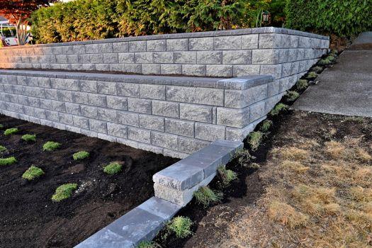 Multi-level stone retaining walls with newly planted shrubs, representing customized hardscaping design.