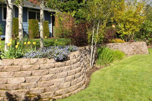 Curved stone retaining wall with flowers and trees, showcasing hardscaping services.