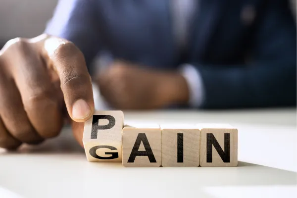 Man turning over alphabet block to change the word pain into the word gain.