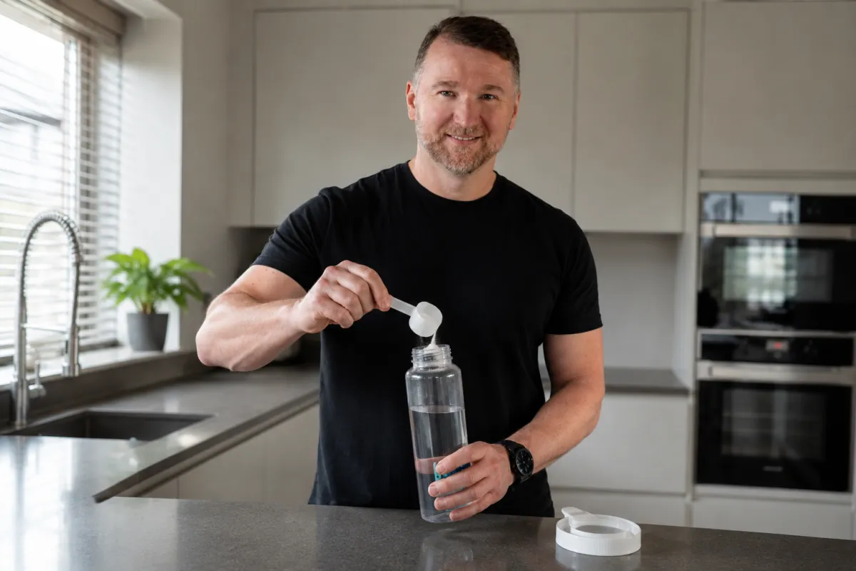 Rob Ede pouring a scoop of creatine in his water bottle, standing in a kitchen. 