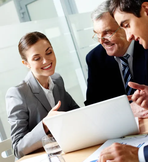 Group of business professionals in a meeting, smiling and reviewing content on a laptop, representing teamwork and digital strategy.