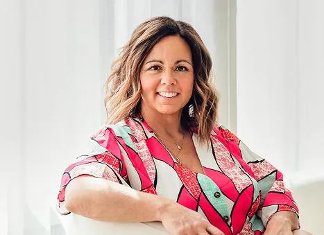 Businesswoman with shoulder-length brunette hair, smiling confidently in a bright patterned blouse.