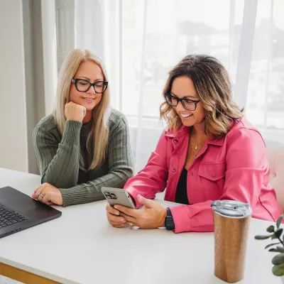Two women at a desk smiling at phone