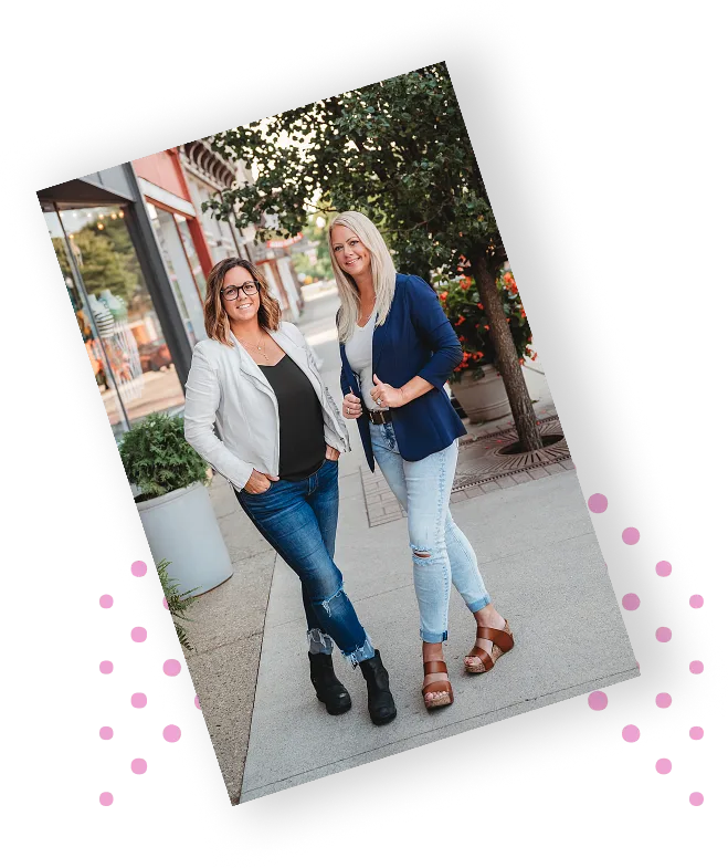 wo entrepreneurs walking side by side on a downtown sidewalk, smiling and dressed in business casual.